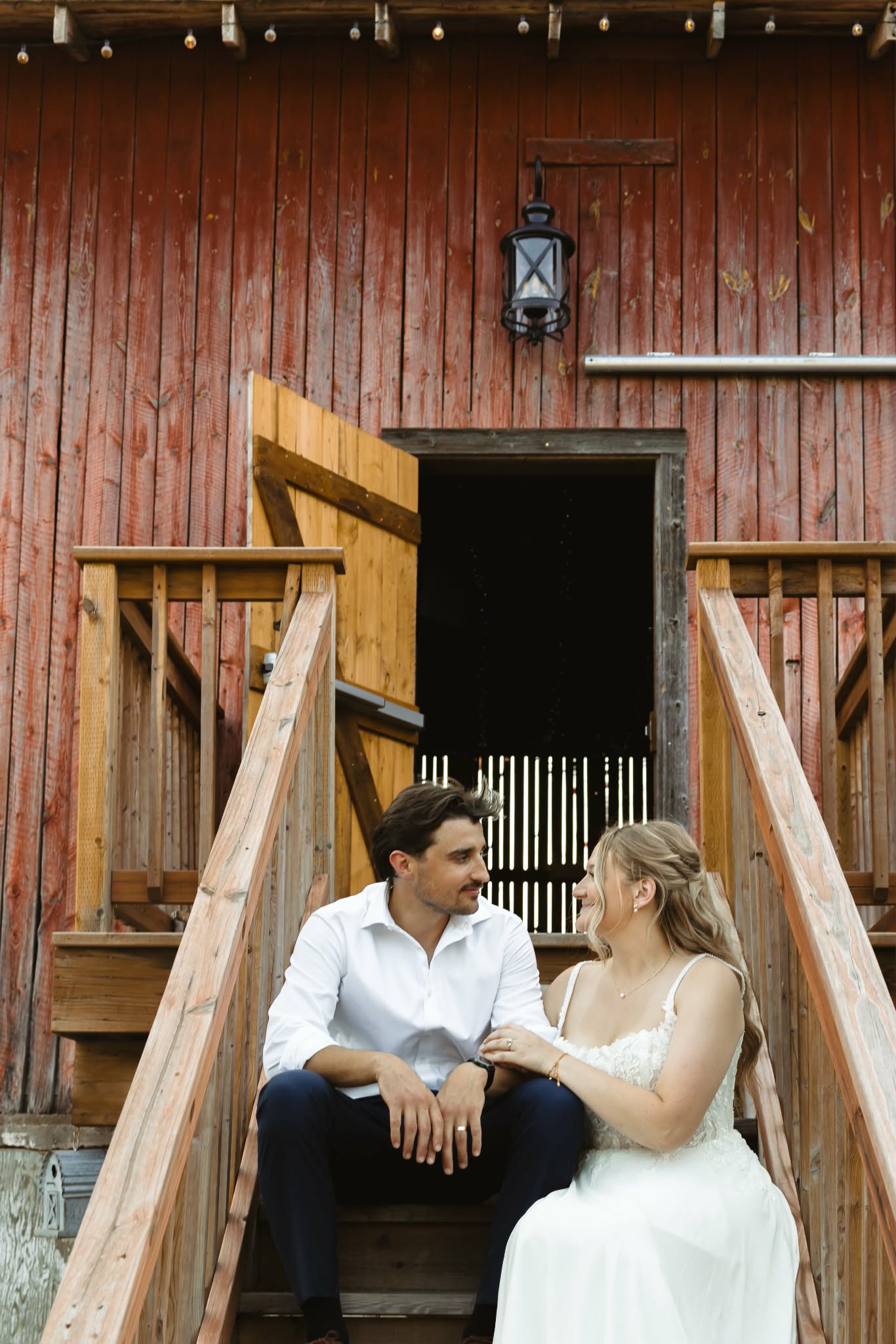 Bride and groom sitting together on the wooden steps of the barn beneath a black lantern