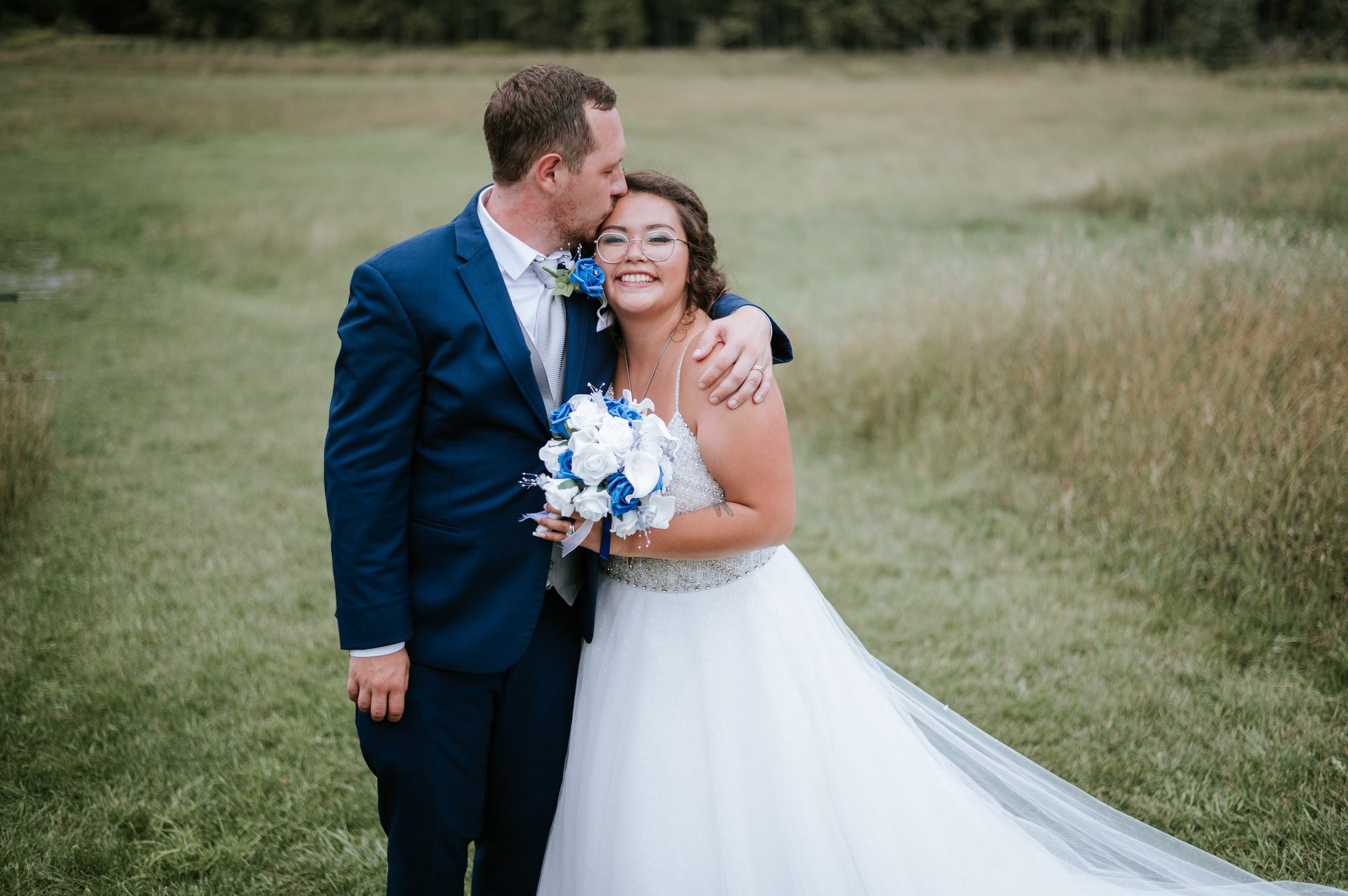 Groom kissing bride on the forehead in a lush green countryside field