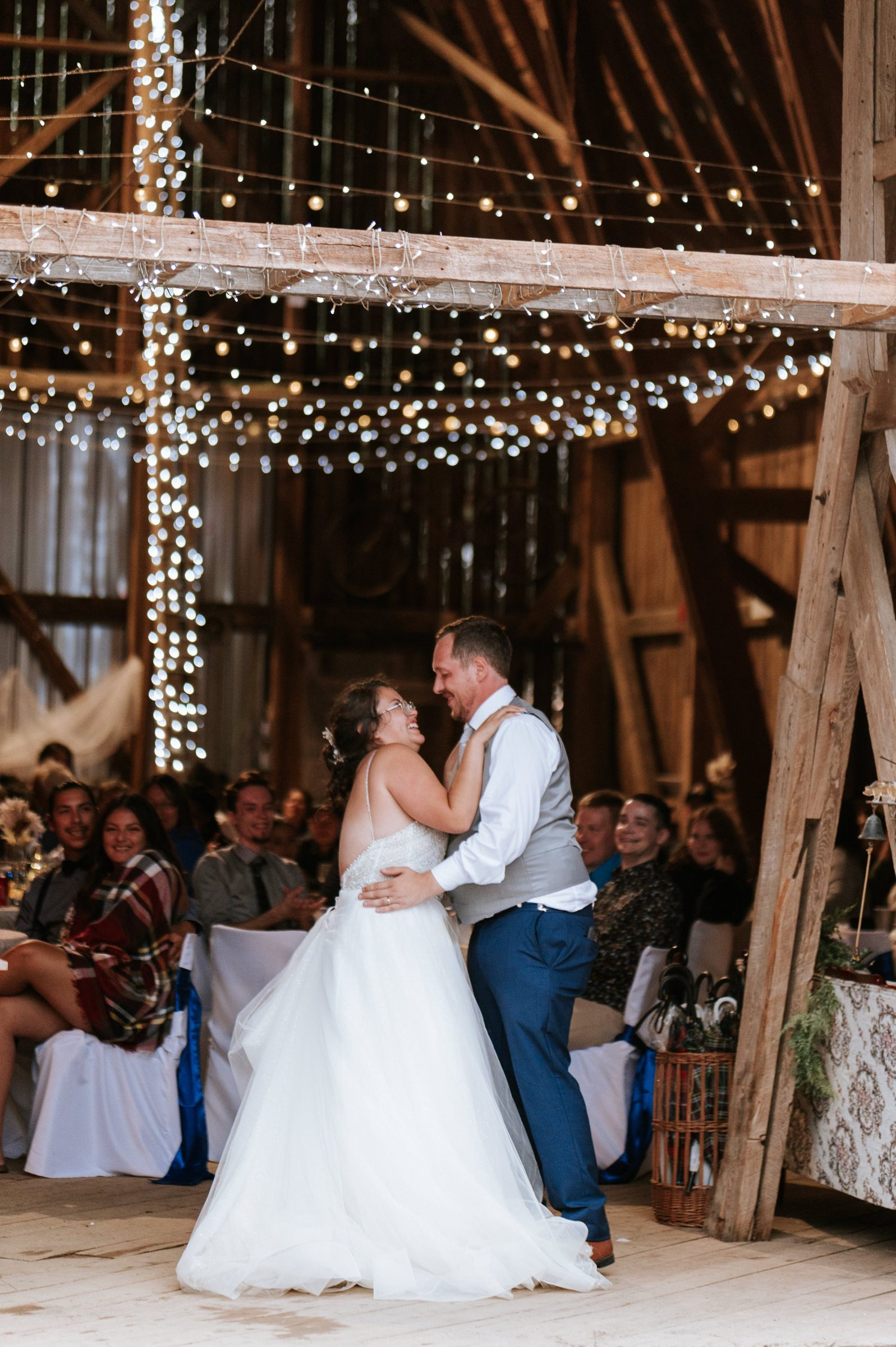 Couple sharing their first dance under cascading fairy lights with exposed barn beams