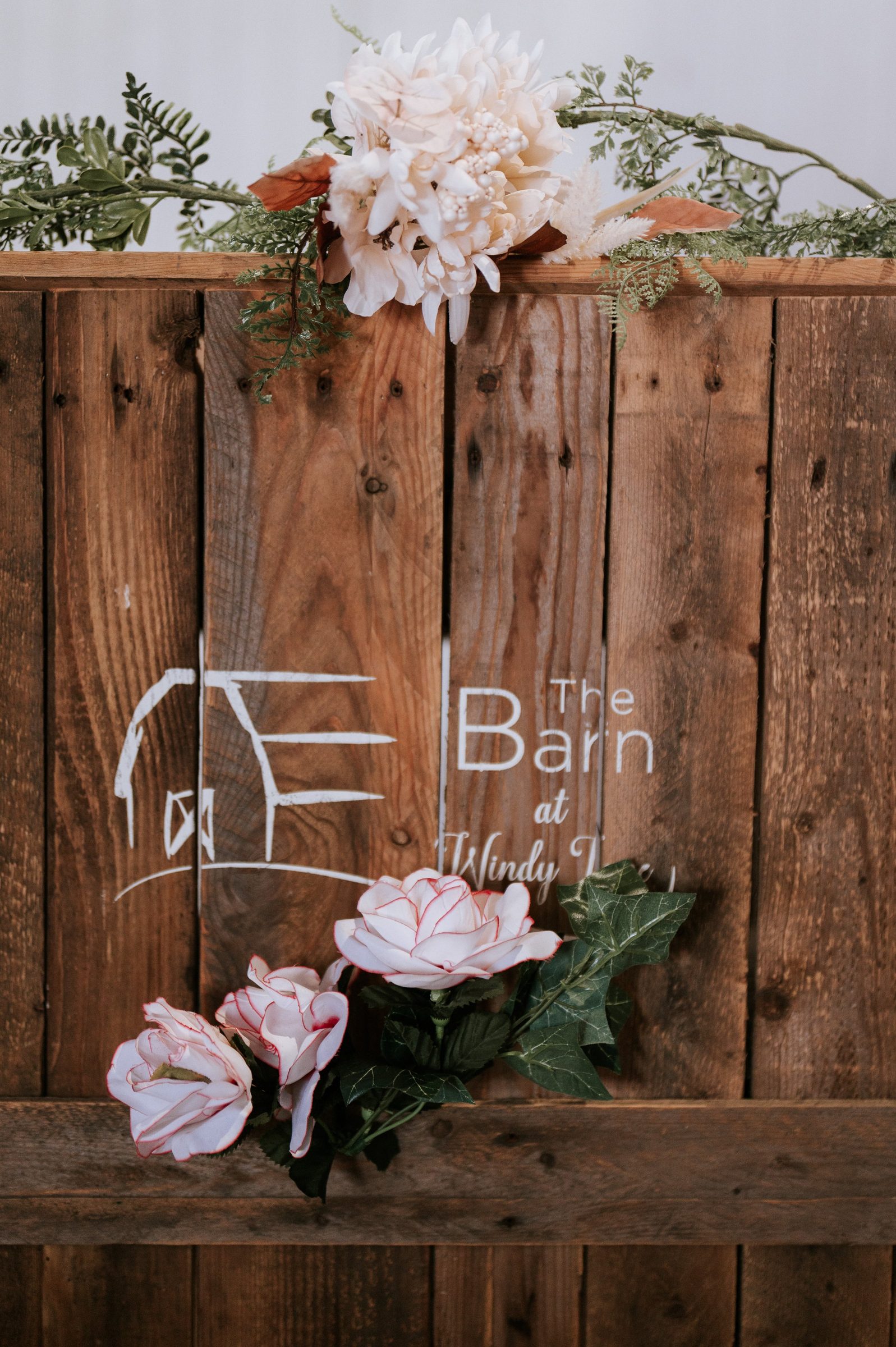 The Barn at Windy Lane logo painted on reclaimed wood with fresh flowers