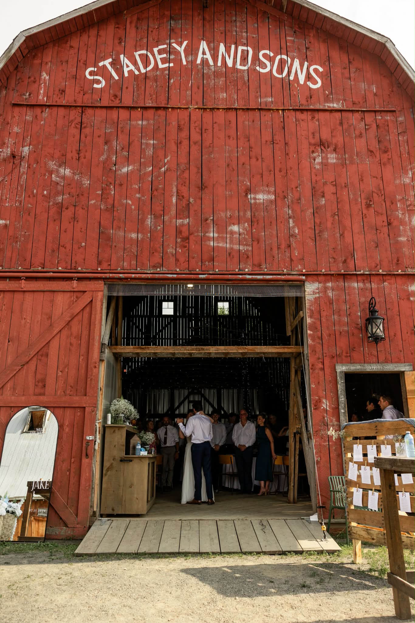 The red barn with STADEY AND SONS painted across the gable, its wide doors open onto a wedding reception inside