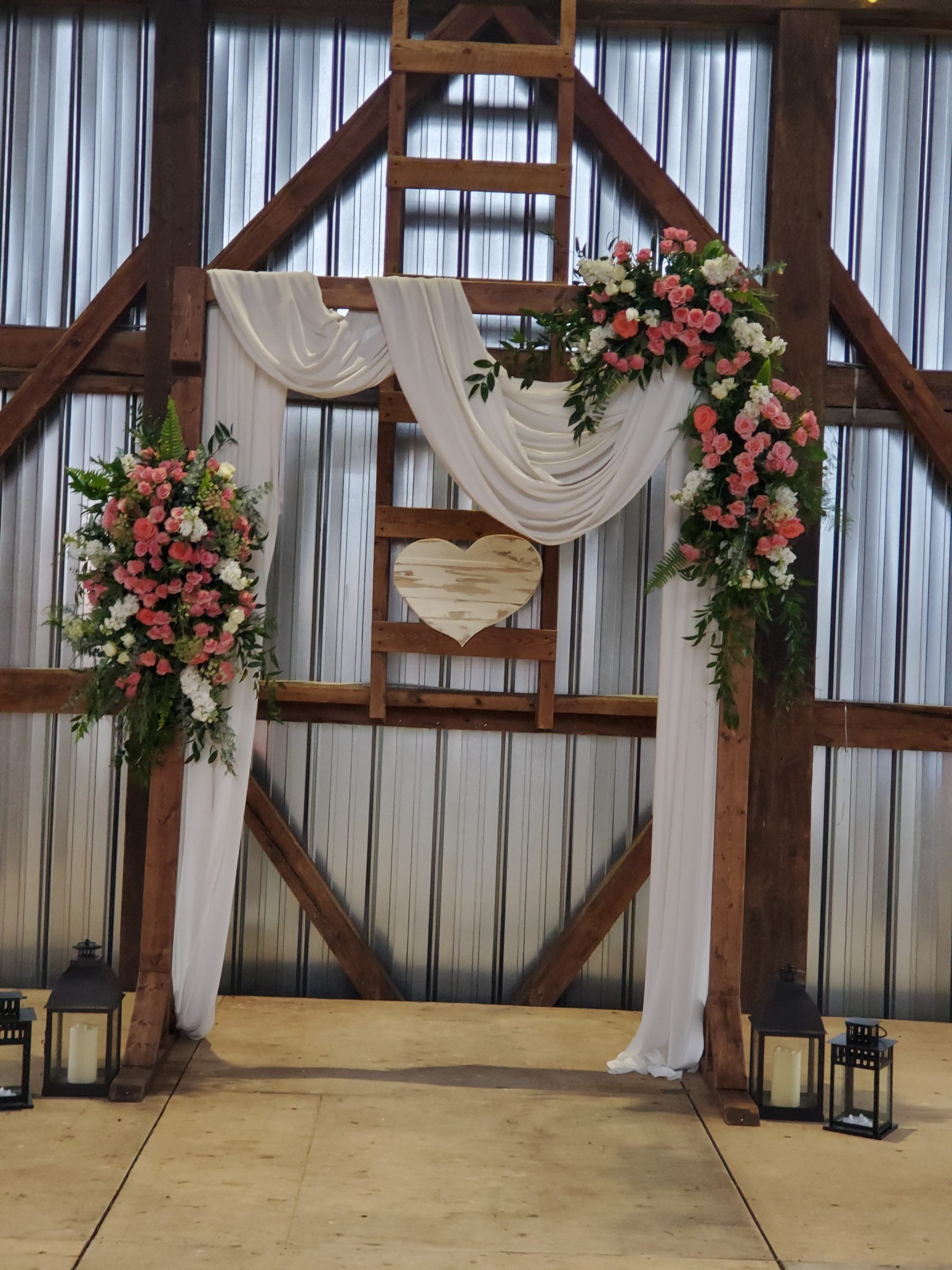 Wedding ceremony arch with white draping and pink flowers