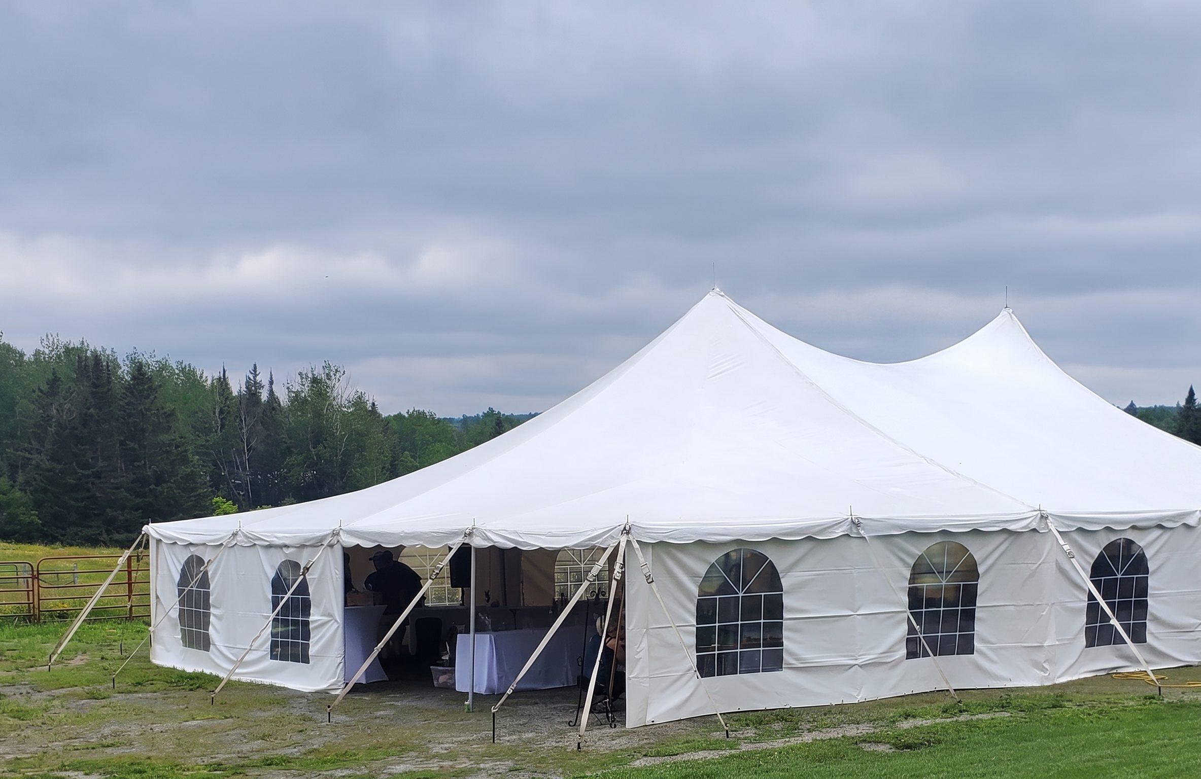 White marquee tent with arched windows set up on the lawn beside the treeline